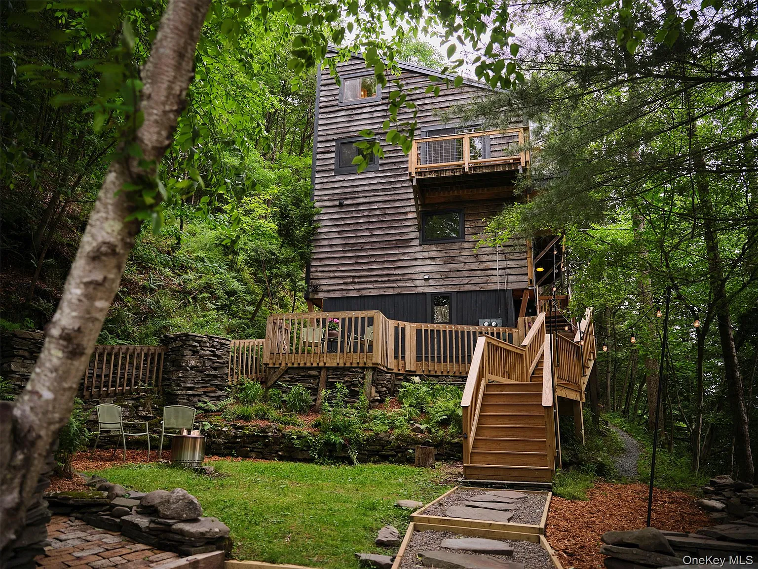 The cabin seen from the yard with stone walls and wooden stairs