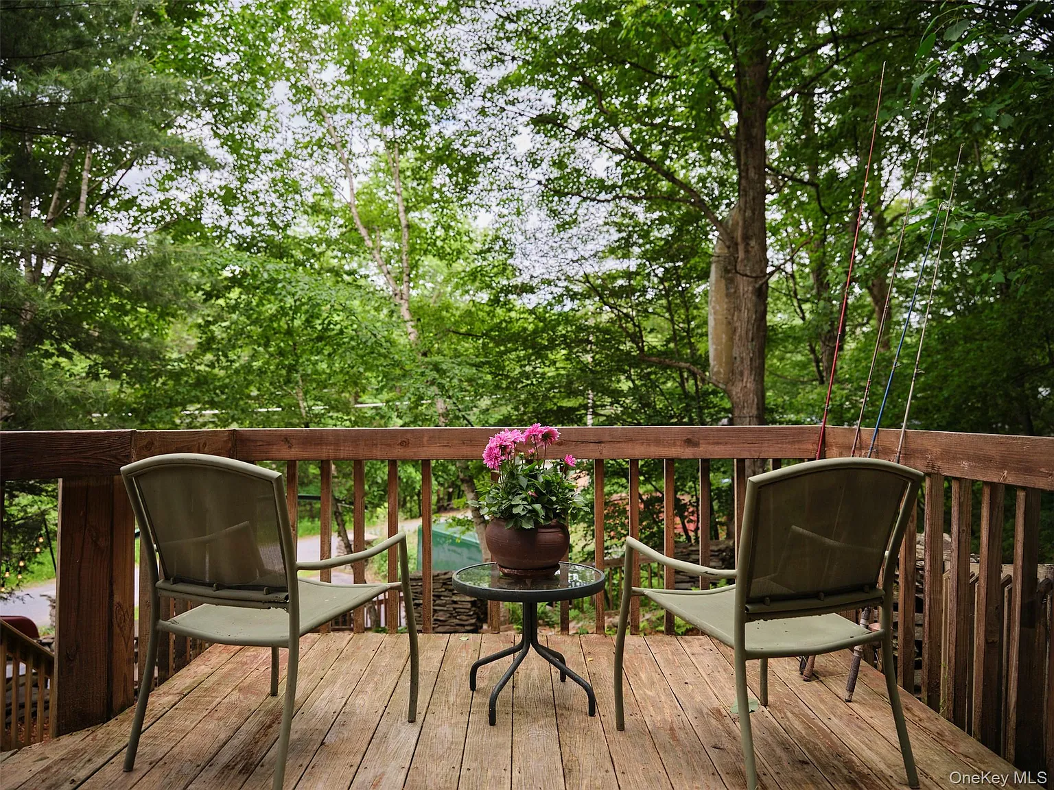 Small deck with two chairs, a flower pot and fishing rods against the railing